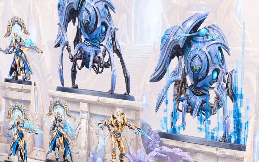 Painted Protoss miniatures in gold and blue: two large stalker walkers, robed adepts and a gold zealot on a white stone temple.