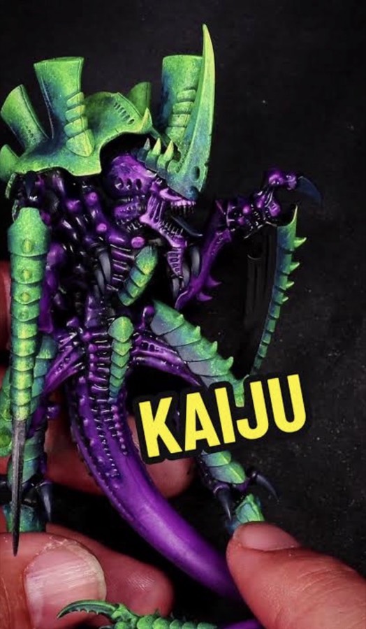 An alien miniature painted in saturated purple with acid-green armor plates, held in a hand, with a yellow "KAIJU" caption over the photo.
